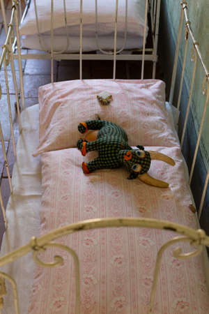 Concept of a sad and poor childhood. Worn old handmade stuffed animal lying on a small rickety bed...