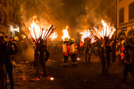 Chienbaese festival. Switzerland, Liestal, Rathausstrasse 25, 18th of February 2018. Festival participants carrying burning broom shaped wooden logs on their shoulders through the old town.のeditorial素材