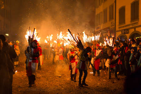 Chienbaese festival. Switzerland, Liestal, Rathausstrasse 25, 18th of February 2018. Festival participants carrying burning broom shaped wooden logs on their shoulders through the old town.のeditorial素材