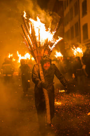 Chienbaese festival. Switzerland, Liestal, Rathausstrasse 25, 18th of February 2018. Festival participants carrying burning broom shaped wooden logs on their shoulders through the old town.のeditorial素材