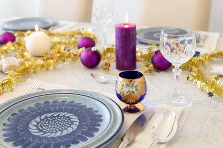 Close-up of a decorated dining table with burning candles, sterling cutlery, crystal glasses,...