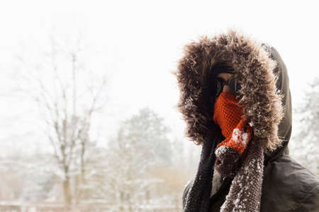 Portrait of a single male winter adventurer wearing a warm green coat with fur hood, a blue ski cap, an orange scarf and black retro style gogglesの写真素材