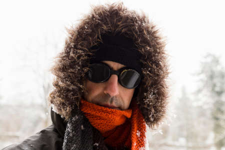 Portrait of a single male winter adventurer wearing a warm green coat with fur hood, a blue ski cap,...