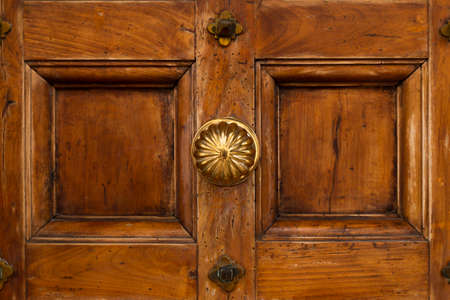 Front view of a vintage brown wooden door with round ornate brass knobの写真素材