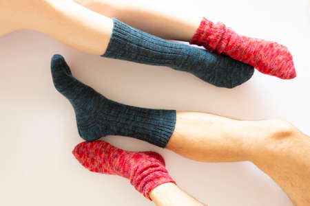 Top view of two pairs of legs wearing a red and a blue sock on white background