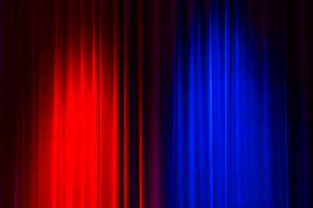 Front view of a closed vintage style velvet theater curtain illuminated by a red and a blue spotlightの写真素材