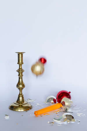 Front view of falling and shattered red and silver Christmas baubles and a bronze candleholder with...