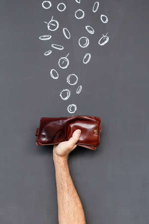 Concept of earning money with a brown leather wallet held in a hand in front of a blackboard with hand drawn coinsの写真素材