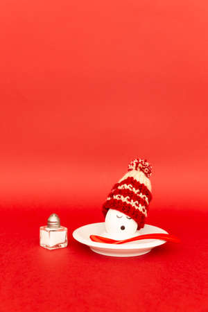 Fun breakfast concept with a boiled egg with abstract sleepy human face wearing a knitted woolen hat on red backgroundの写真素材