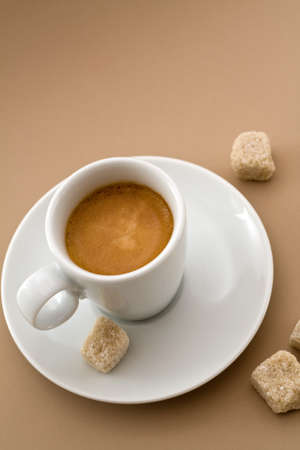 Espresso cup with sugar cubes over a light brown background,