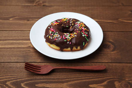 chocolate frosted doughnut on plate on wooden tableの写真素材