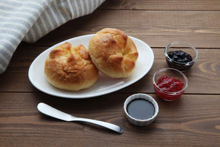 butter bread roll on a plate with strawberry jam on wooden tableの写真素材