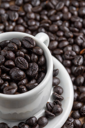 Aerial view of half a white cup and saucer with coffee beans, over more beans, selective focus, verticalの写真素材