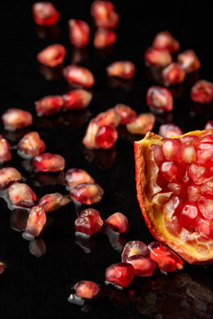 Close-up of white colander with wet red pomegranate, seeds out of focus, on black background, verticalの写真素材