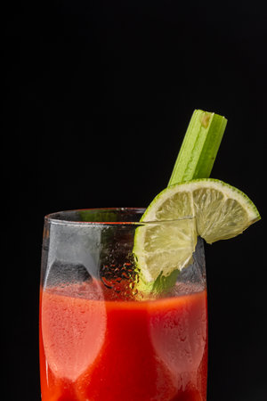 Close-up of glass of Bloody Mary cocktail with lime and celery, on black background in vertical, with copy spaceの写真素材
