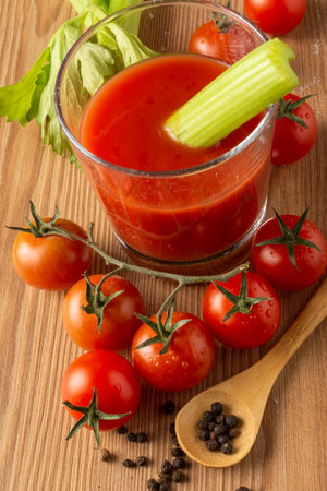 Aerial view of glass with tomato and celery juice, on wooden table with cherry tomatoes, pepper and wooden spoon, selective focus, verticalの写真素材