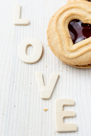 Aerial view of heart-shaped cookie on white table and crumbs with the word love, verticalの写真素材