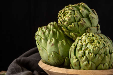 Close-up of green artichokes in wooden bowl and black cloth, with selective focus, black background, horizontal, with copy spaceの写真素材