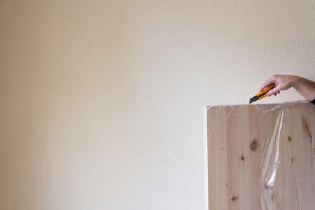 View of woman's hand with cutter unpacking a pine board, on a wall, horizontallyの写真素材