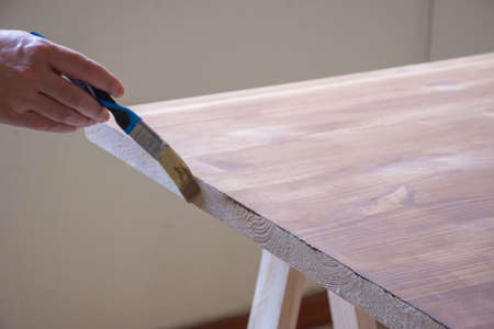 View of woman's hand with brush going over the paint on a pine wood table, horizontalの写真素材