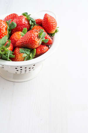 Aerial view of strawberries in a white colander, on white wooden table, vertically, with copy spaceの写真素材