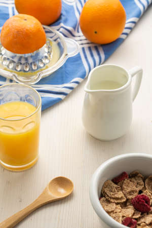 Aerial view of cereal bowl, spoon, oranges, juicer, cloth, jug with milk and glass with orange juice, on white wood, verticalの写真素材
