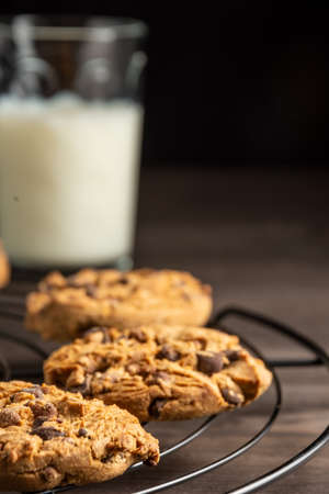 Close-up of chocolate cookies on wire rack, glass of milk, selective focus, on wooden table,...