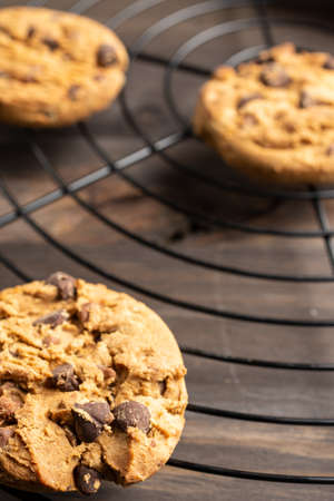 Top view of three chocolate chip cookies on wire rack, selective focus, on wooden table, vertical