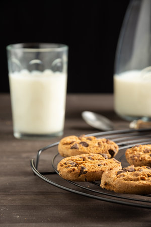 Close-up of cookies on wire rack, wooden table with glass and bottle of milk, selective focus, black background, verticalの写真素材