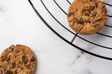 Close-up of two chocolate cookies on black rack, on white marble table, selective focus, horizontal