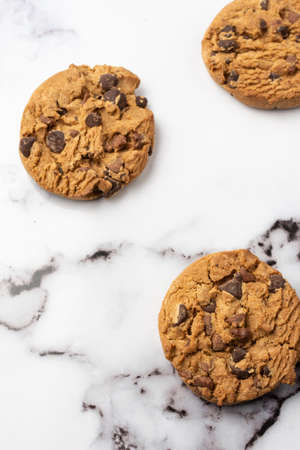 Aerial view of three chocolate chip cookies on white marble table, selective focus, vertical, with copy spaceの写真素材