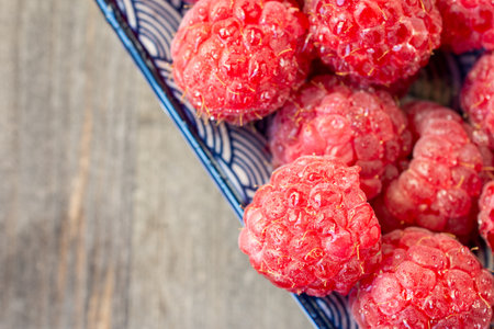 Diagonal aerial view of wet raspberries on blue plate, selective focus, on dark wooden table, horizontal, with copy spaceの写真素材