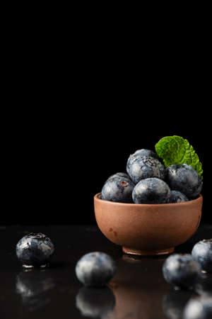 Close-up of blueberries out of focus, bowl with blueberries and mint leaf, on black slate with reflection, black background, vertical, with copy spaceの写真素材