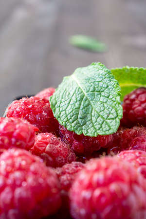 Close-up of mint leaf, wet raspberries in bowl, selective focus, on dark wooden table, vertical, with copy spaceの写真素材