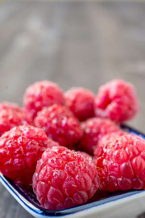Top view of wet raspberries in bowl, selective focus, on dark wooden table, vertical, with copy...