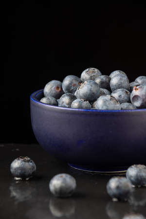 Closeup of blueberries out of focus, blue bowl with blueberries, on black slate with reflection, black background, vertical, with copy spaceの写真素材