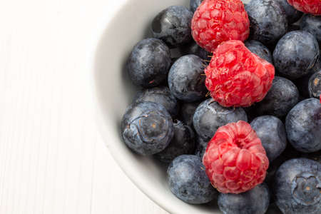 Aerial view of white bowl with blueberries and raspberries, on white table, horizontalの写真素材
