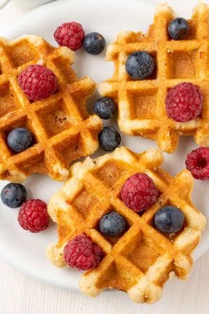 Aerial view of three waffles with raspberries and blueberries on white plate, selective focus, verticalの写真素材