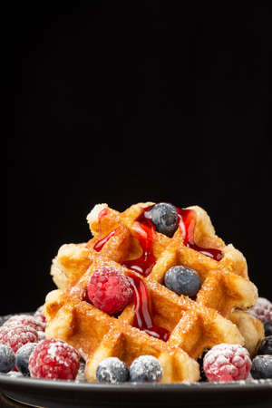 Close-up of waffle with raspberries and blueberries with strawberry syrup, black background, vertical, with copy spaceの写真素材