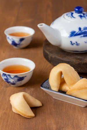 Top view of fortune cookies on a plate, teapot and Chinese cups with tea, on wooden table, with selective focus, verticalの写真素材