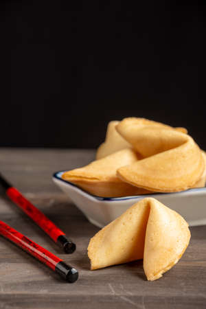 Close-up of fortune cookies on saucer and chopsticks, on dark wooden table, selective focus, black background, vertical, with copy spaceの写真素材