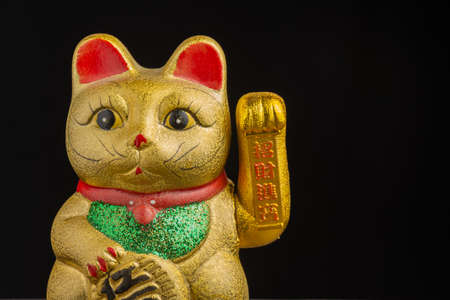 Close-up detail of golden maneki neko with green and red tones, black background, horizontal, with copy spaceの写真素材