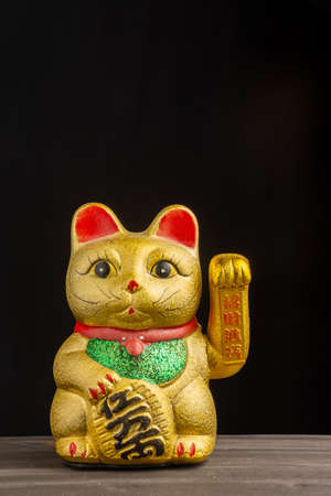 Close-up of golden maneki neko on wooden table and black background, vertical, with copy spaceの写真素材