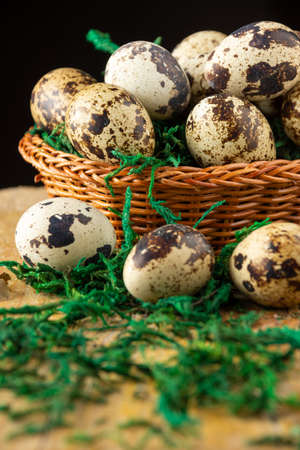Top view of quail eggs in basket, selective focus, on rustic wooden table with green grass, black background, verticalの写真素材