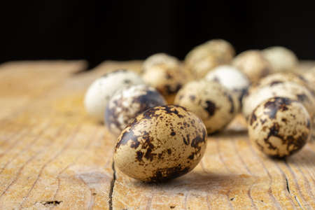 Close-up of a group of quail eggs, selective focus, on wooden table and black background, horizontal, with copy spaceの写真素材