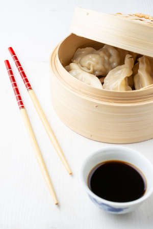 Top view of steamer with gyozas, soy sauce in bowl and chopsticks, on white wood, in verticalの写真素材