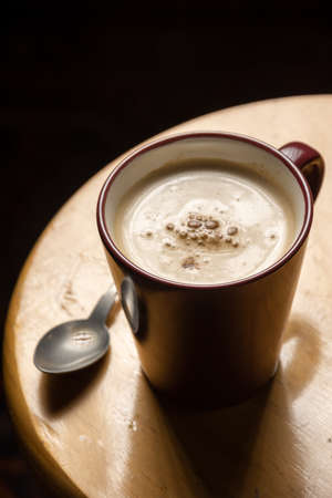 Aerial view of cup of cappuccino coffee and spoon on wooden stool, on black background, in vertical, with copy spaceの写真素材