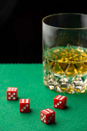 Top view of red dice on green baize with glass of whiskey, defocused, black background, vertical, with copy spaceの写真素材