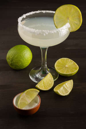 Top view of margarita cocktail glass with lime slices and salt, on wooden table with cut limes, verticalの写真素材