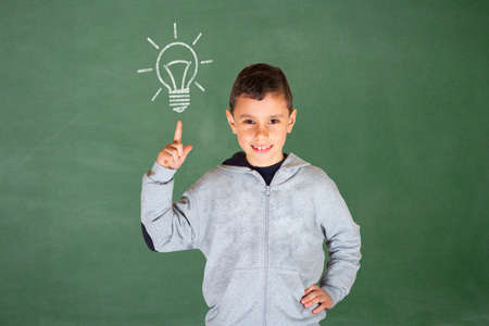 Conceptual portrait - Cute boy in front of a green chalkboard pointing up to a light bulbの写真素材